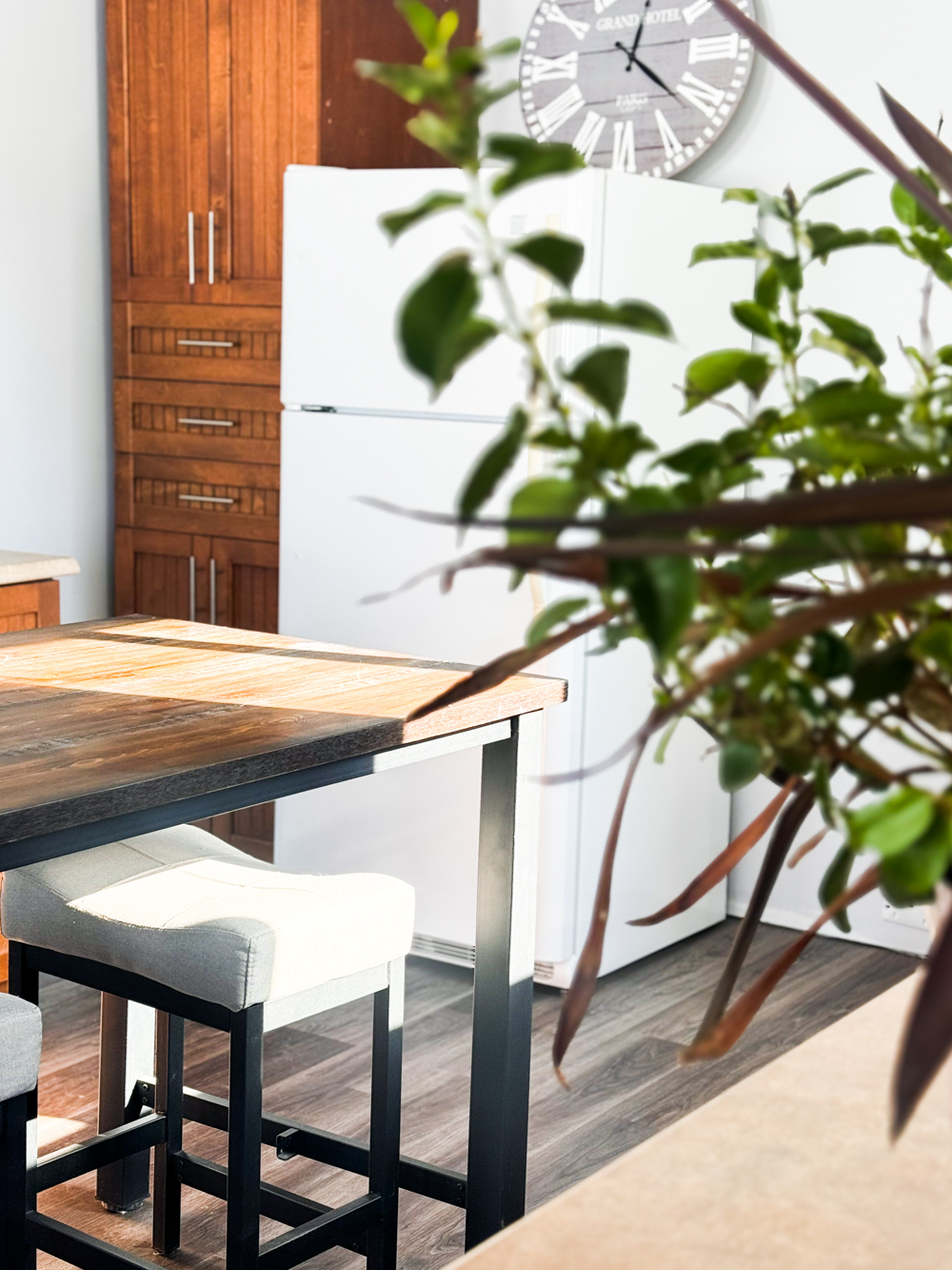 Cuisine partagée lumineuse avec table haute, tabourets et réfrigérateur, accessible pour les personnes qui louent une salle ou un bureau dans l’espace.