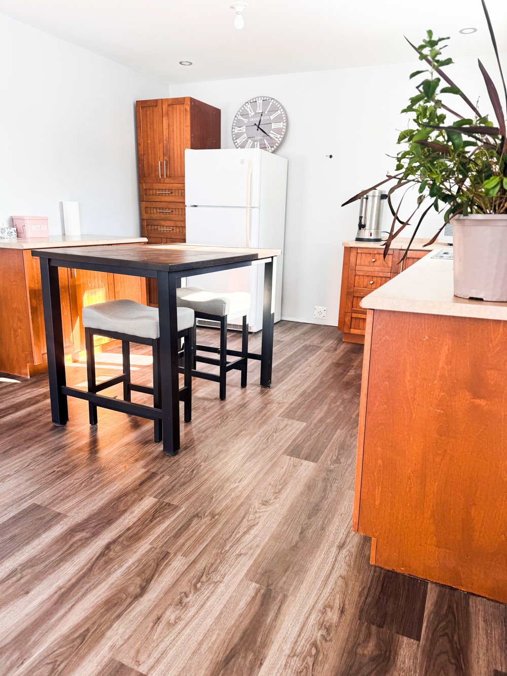 Cuisine partagée lumineuse avec table haute, tabourets et réfrigérateur, accessible pour les personnes qui louent une salle ou un bureau dans l’espace.