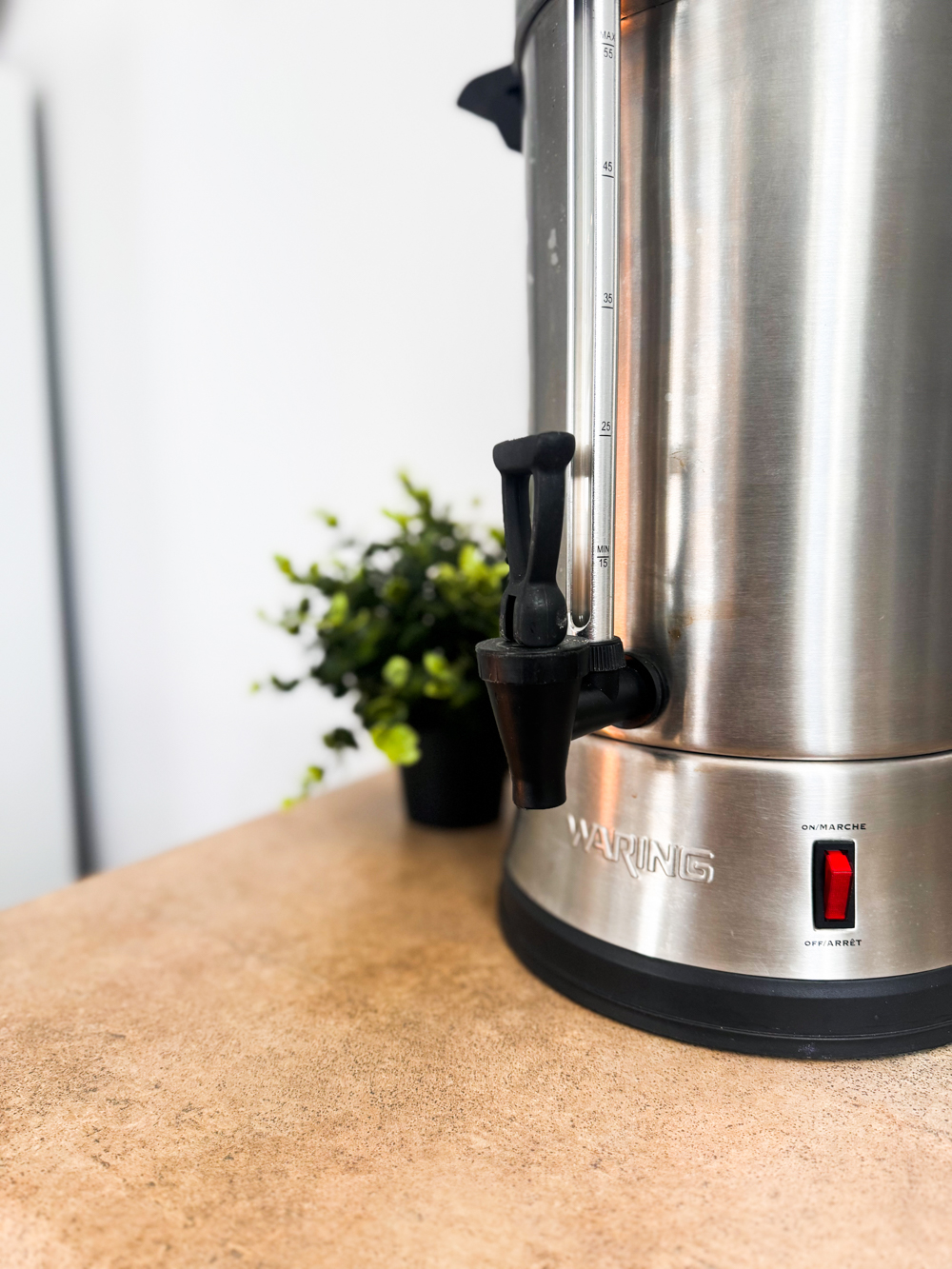 Cuisine partagée lumineuse avec table haute, tabourets et réfrigérateur, accessible pour les personnes qui louent une salle ou un bureau dans l’espace.